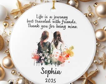 May include: White ceramic ornament with a gold string for hanging. The ornament features a watercolor illustration of two figures and the text: "Life is a journey best traveled with friends. Thank you for being mine. Sophia 2025."