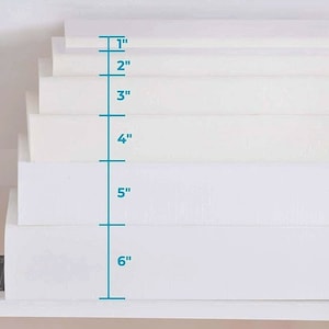 May include: A stack of six white rectangular boxes with a ruler measuring 6 inches in height.