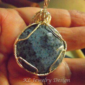 May include: A silver wire wrapped pendant featuring a round, blue and gray stone with a speckled pattern.