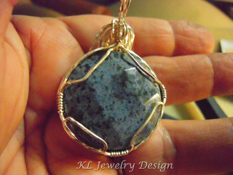 May include: A silver wire wrapped pendant featuring a round, blue and gray stone with a speckled pattern.