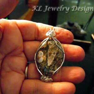 Peut inclure: Un pendentif en fil d'argent enveloppé avec une pierre d'agate brune et blanche au motif unique. Le pendentif est tenu dans une main.