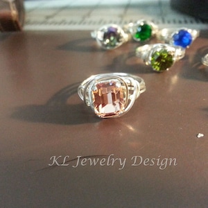 Könnte beinhalten: Ein silberner Ring mit einem pfirsichfarbenen Edelstein, der in einem drahtgewickelten Design gefasst ist. Der Ring liegt auf einer braunen Oberfläche mit dem Text "KL Jewelry Design".