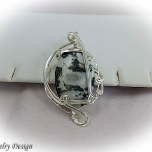 May include: A silver wire wrapped pendant featuring a black and white agate stone. The stone has a unique pattern of black and white swirls.