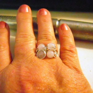 Może przedstawiać: Srebrny pierścionek z drutu z czterema różowymi i białymi kamieniami. Pierścionek jest na palcu.