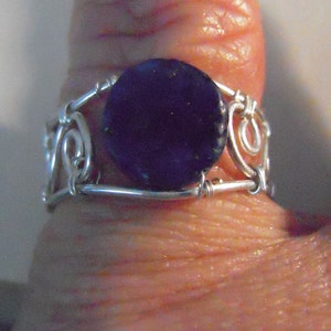 Pode incluir: Um anel de prata com uma pedra de vidro roxo escuro engastada em um design de arame.