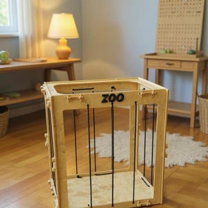 Op de afbeelding: Een houten speelstructuur met het woord "ZOO" op de voorkant. De structuur heeft een kooi-achtig ontwerp met zwarte verticale staven. Het frame is gemaakt van lichtgekleurd hout. De structuur is ontworpen voor kinderspel.
