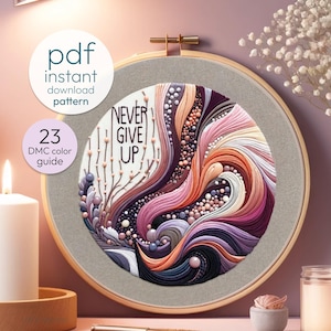 May include: A circular embroidery hoop with a colorful abstract design featuring swirls and dots. The design includes the text "NEVER GIVE UP" in a white font. The hoop is on a pink background.
