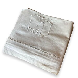 May include: Folded white linen sheet with embroidered initials "GO" in the upper corner. The sheet has a decorative stitched border along the edge. The fabric appears to be slightly off-white.