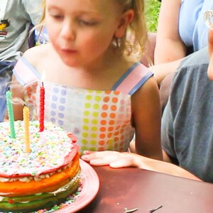 Image shows a child blowing out the candles on her birthday cake. The candles are all rolled beeswax birthday candles handmade by Pumpkin Plus Bear.