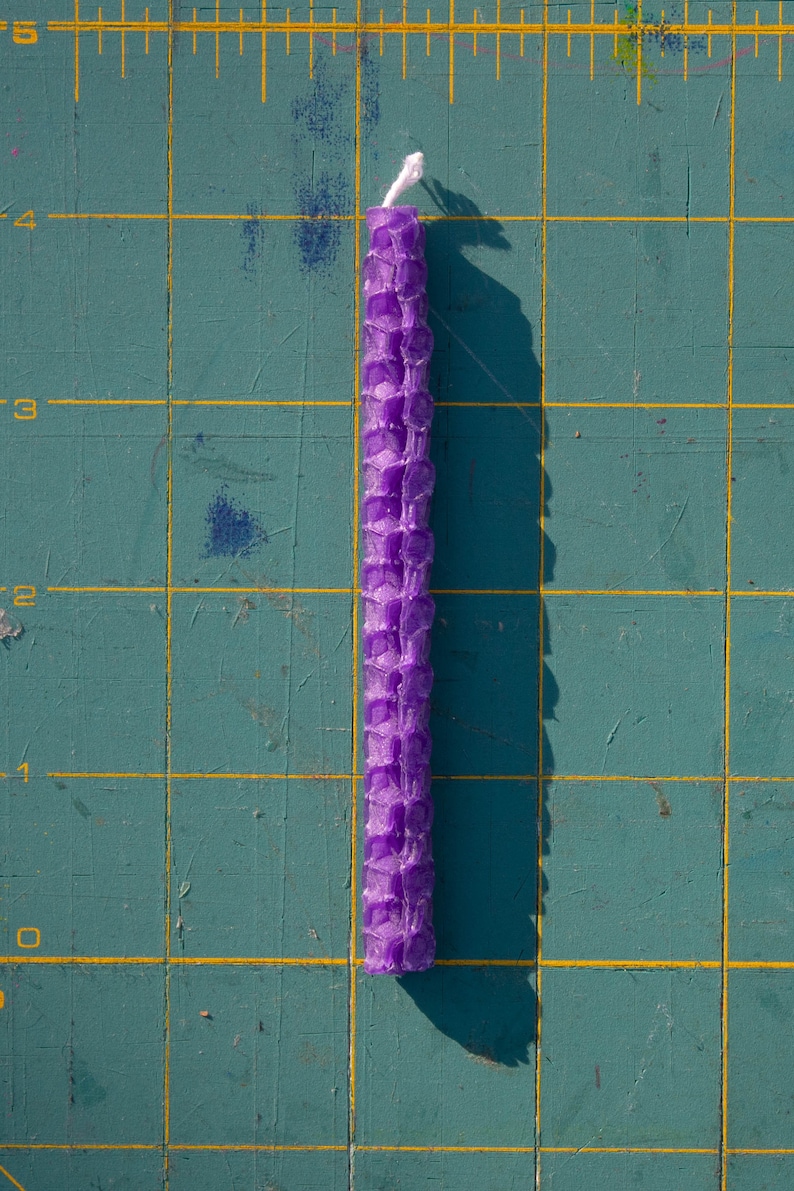 Image shows one candle lying on a mat marked with measurements. Each candle is four inches long.