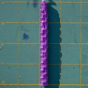 Image shows one rolled beeswax birthday candle on a cutting mat with measurements marked. Each candle is approximately four inches tall by one quarter inch wide.