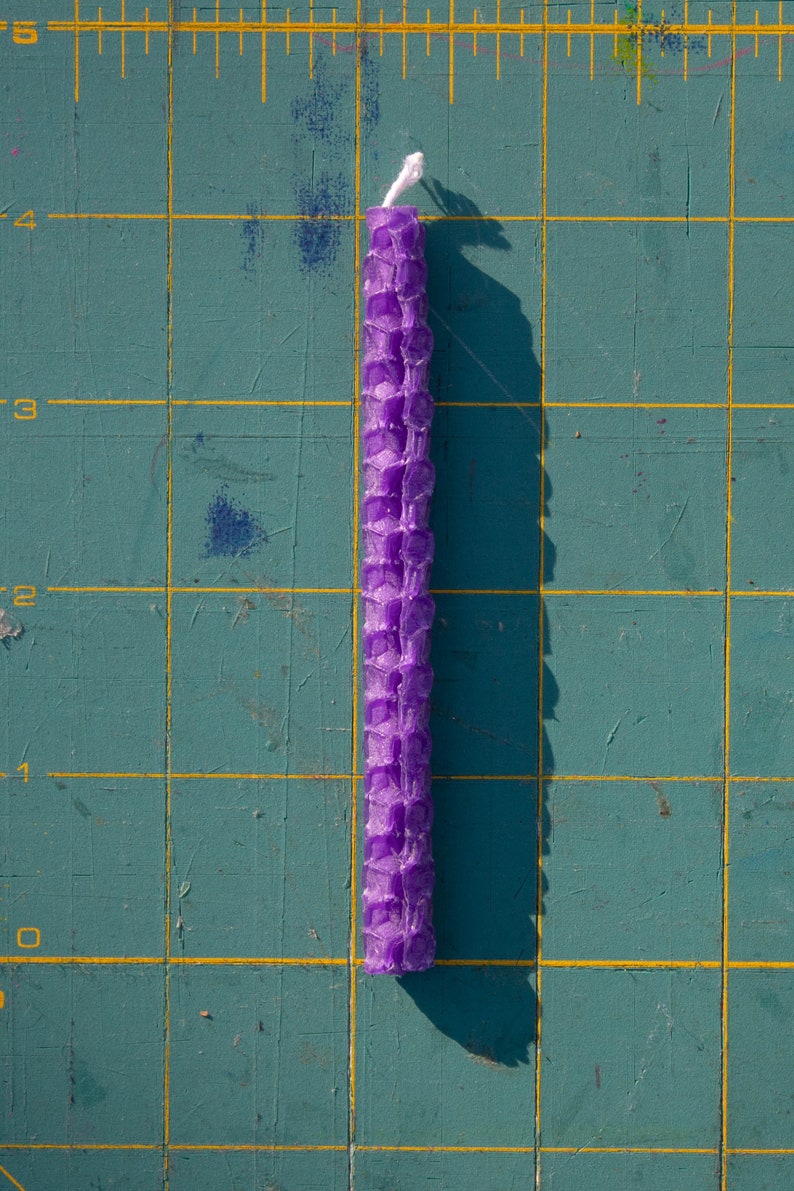 Image shows one rolled beeswax birthday candle on a cutting mat with measurements marked. Each candle is approximately four inches tall by one quarter inch wide.