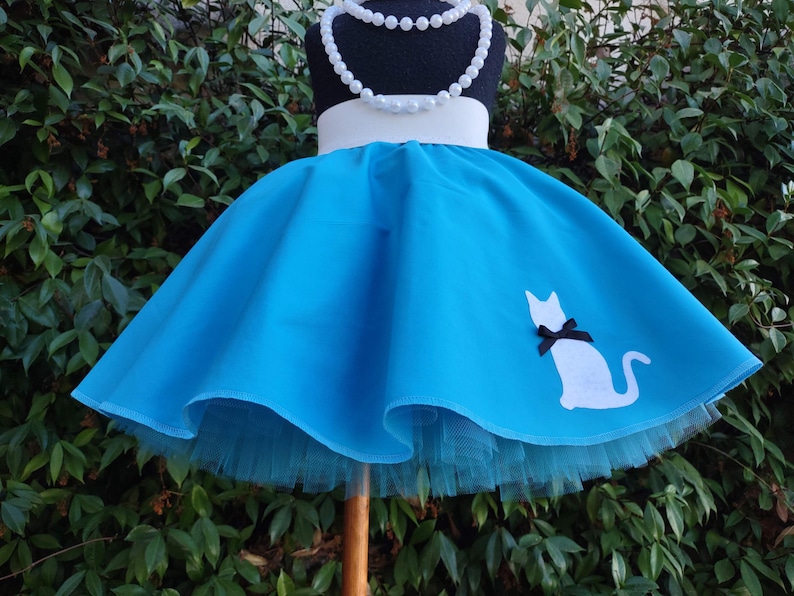 K&ouml;nnte beinhalten: Ein blauer T&uuml;llrock mit einer wei&szlig;en Katzen-Silhouette und einem wei&szlig;en Bund. Der Rock ist auf einem Mannequin und hat einen wei&szlig;en T&uuml;ll-Unterrock.