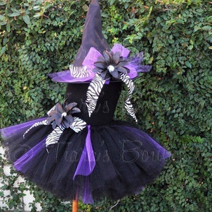 May include: Black and purple tulle tutu with a black witch hat and zebra print ribbon. The hat has a large purple flower with a rhinestone center.