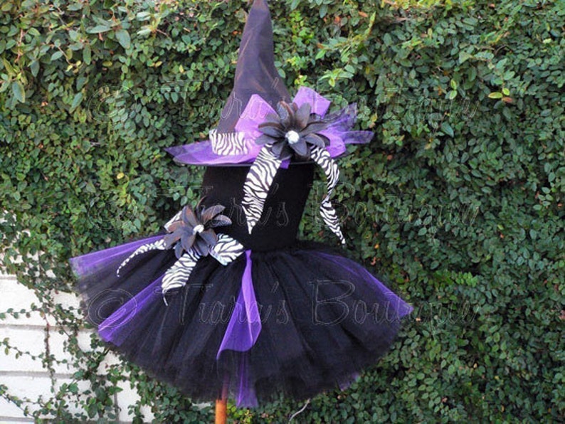 May include: Black and purple tulle tutu with a black witch hat and zebra print ribbon. The hat has a large purple flower with a rhinestone center.