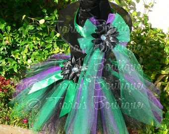May include: A black witch hat with a green and purple tulle tutu. The hat has a black velvet brim and a tall pointed crown. The tutu is decorated with black satin ribbon and a large black flower with a rhinestone center.