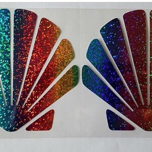 May include: Two iridescent rainbow glitter seashell stickers. Each sticker is shaped like a seashell with a fan-like design. The stickers are perfect for adding a touch of sparkle to any project.