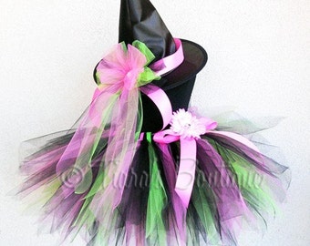 May include: A black witch hat with a pink and green tulle tutu. The hat has a pink ribbon and a pink flower with a white center.