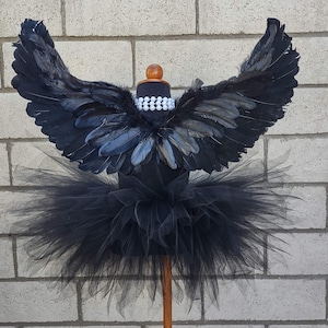 May include: Black tulle tutu with black feather wings. The tutu is on a mannequin with a pearl necklace.