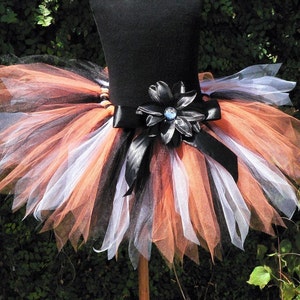 May include: A black, white, and orange tulle tutu with a black satin ribbon and a black flower with a blue rhinestone center.