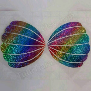 May include: Two iridescent rainbow glitter seashell shapes. The shells are outlined in white and have a holographic finish.