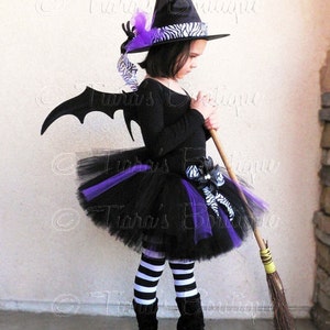 May include: A child dressed as a witch for Halloween. The costume includes a black tutu with purple and zebra print accents, a black witch hat with a zebra print band, black and white striped tights, and black boots. The child is holding a broom.