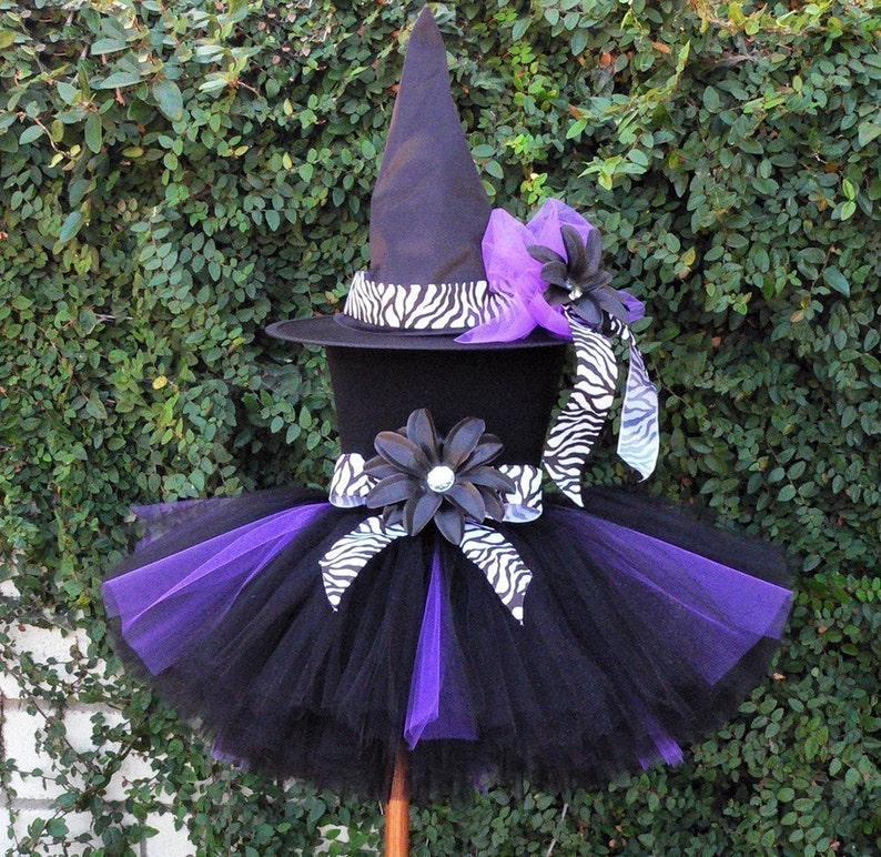 May include: A black and purple tutu with a black witch hat with a zebra print band and a purple flower. The hat has a black and white zebra print ribbon.