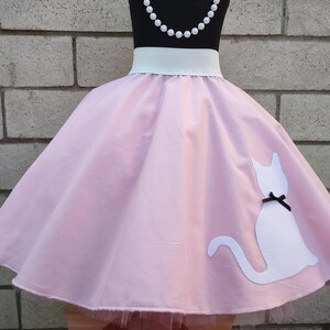 K&ouml;nnte beinhalten: Ein rosa Kreisrock mit einem wei&szlig;en Bund und einer wei&szlig;en Katzen-Silhouette auf der R&uuml;ckseite. Die Katze hat eine schwarze Schleife.