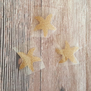 May include: Three gold glitter starfish on clear adhesive sheets.