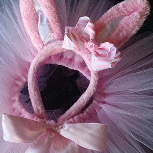 May include: Pink tulle tutu with a pink bunny ear headband and a pink satin bow. The headband has a white and pink striped bow.