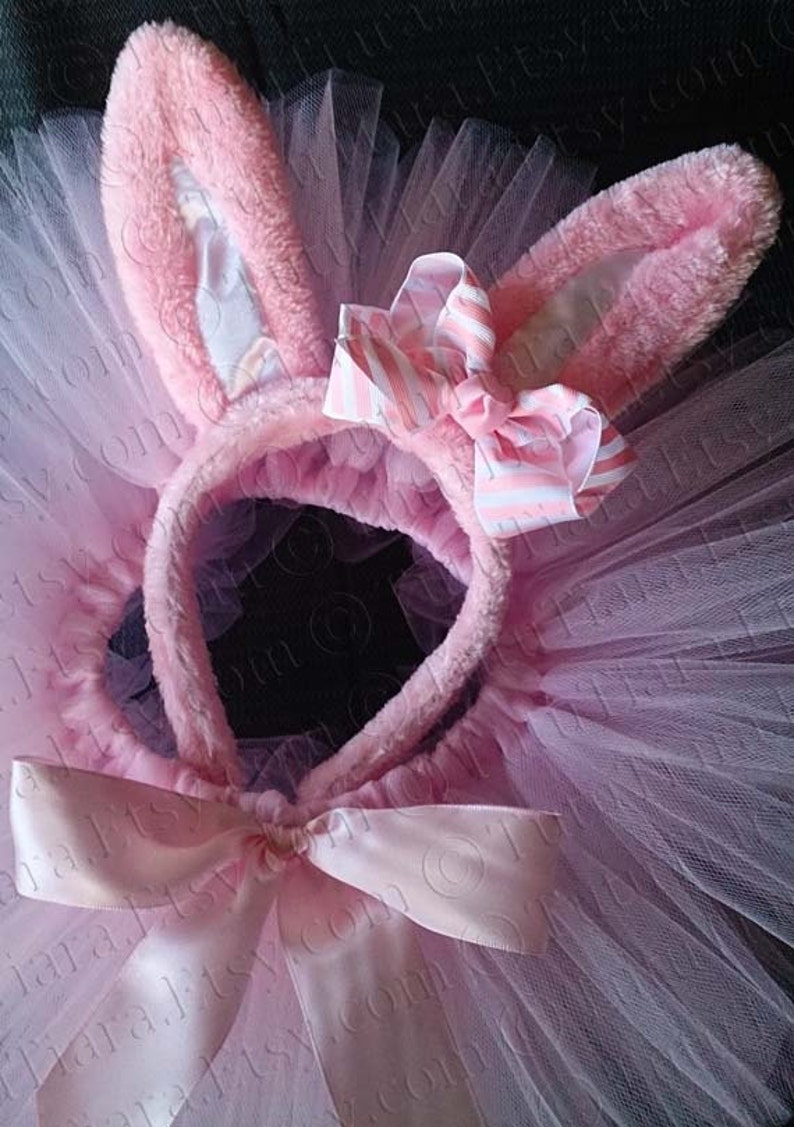 May include: Pink tulle tutu with a pink bunny ear headband and a pink satin bow. The headband has a white and pink striped bow.