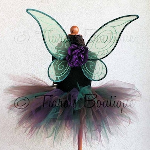 May include: A fairy costume set on a mannequin. The set includes a black bodice, a layered tutu skirt in shades of purple, teal, and brown, and teal-colored fairy wings with a swirl design. A purple flower is attached to the bodice.