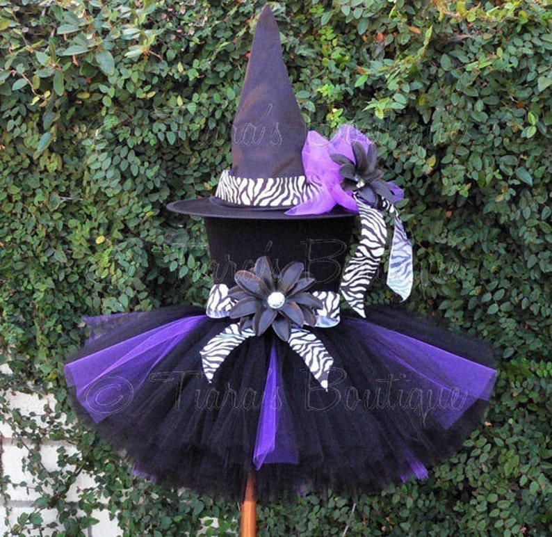 May include: Black and purple tutu with a black witch hat with a zebra print band and a purple flower. The hat has the text "Tara's Boutique" on it.
