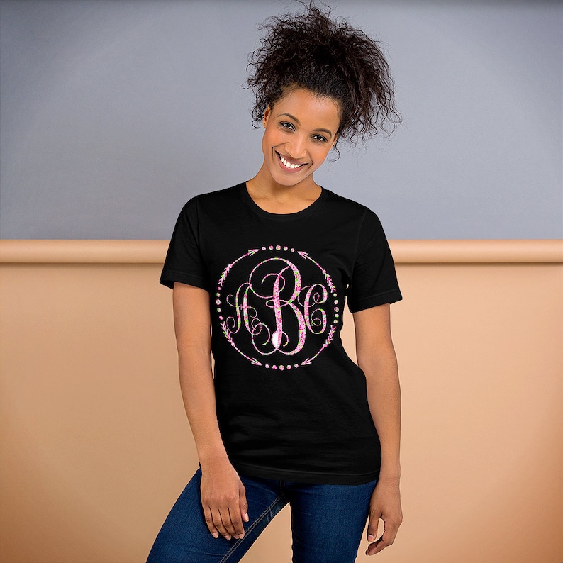 May include: A black t-shirt with a pink and green monogram design in a circle with arrows and dots. The monogram is "ABC".