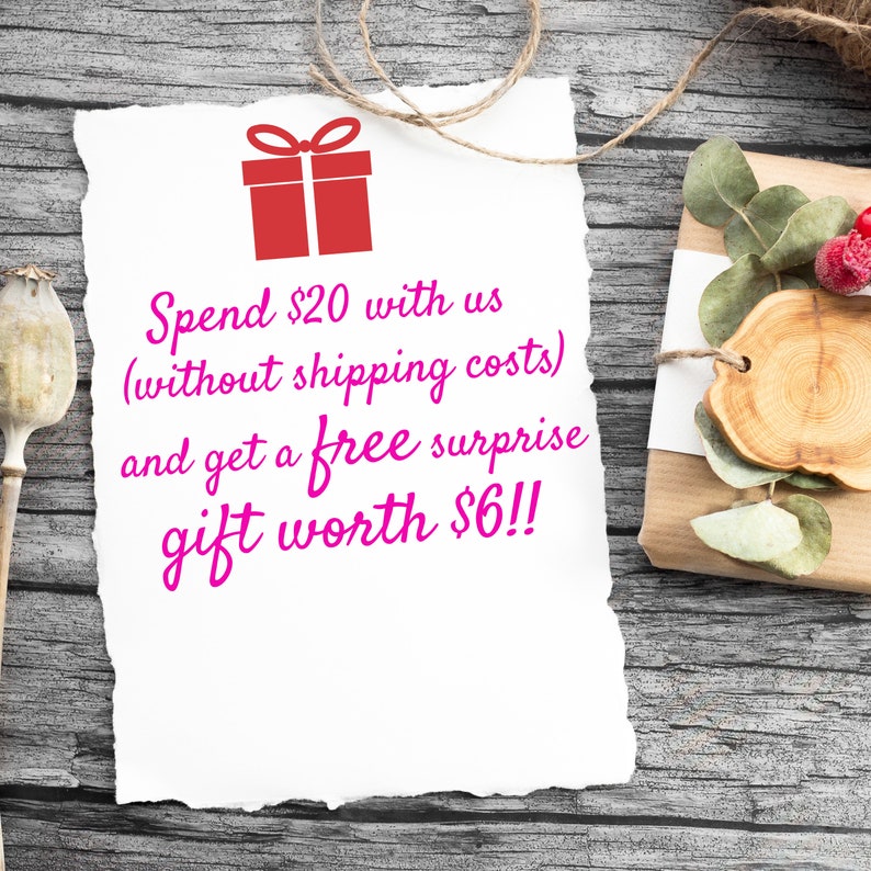 May include: A white paper note with torn edges on a wooden surface. The note has pink text that reads "Spend $20 with us (without shipping costs) and get a free surprise gift worth $6!!". A red gift box icon is above the text.