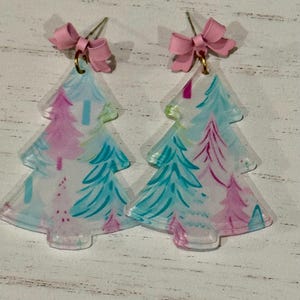 May include: A pair of pink and blue Christmas tree earrings with a pink bow on each earring.