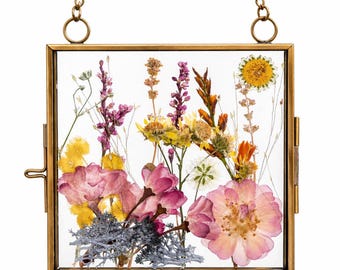 May include: Square brass-framed glass display case with a chain for hanging. The case contains a variety of dried flowers in shades of pink, yellow, and purple. The flowers are arranged against a white background.