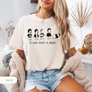 Puede incluir: Camiseta de color marfil con un gr&aacute;fico de cinco patos de dibujos animados con peinados y ropa punk en blanco y negro. El texto "it was never a phase" est&aacute; impreso debajo en una fuente g&oacute;tica. La camiseta tiene un corte holgado.