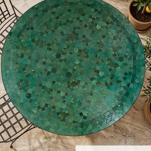 Puede incluir: Una mesa redonda con un tablero de mosaico compuesto por numerosas piezas pequeñas de formas irregulares en varios tonos de verde esmeralda y bosque. La superficie muestra un patrón geométrico complejo con un borde. El texto Andalustreasures es visible.