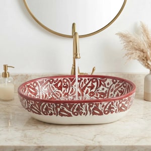 Könnte beinhalten: Ovales Keramik-Waschbecken mit rotem Blumenmuster auf weißem Grund. Das Waschbecken hat einen roten Rand und ist auf einer Marmorarbeitsplatte montiert. Ein goldener Wasserhahn lässt Wasser in das Waschbecken fließen.