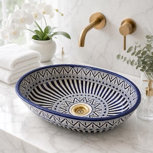 May include: An oval vessel sink featuring a deep blue and white geometric pattern with radiating lines and intricate border designs. The sink includes a central gold-toned drain fixture, contrasting with the dark blue rim and white interior base.