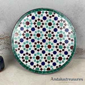 Puede incluir: Mesa redonda de mosaico con un patrón geométrico en blanco, turquesa, burdeos y azul marino. Tiene un borde verde y un borde negro. El texto "Andalustreasures" está en la parte inferior. Diámetro aproximado 60 cm.