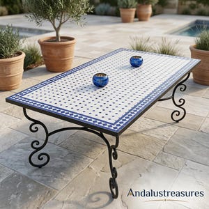 Può includere: Un tavolino rettangolare con piano in mosaico bianco e blu a motivo geometrico e base in ferro battuto nero con gambe a voluta. Due piccoli portacandele rotondi in vetro blu scuro sono posizionati sulla superficie piastrellata.