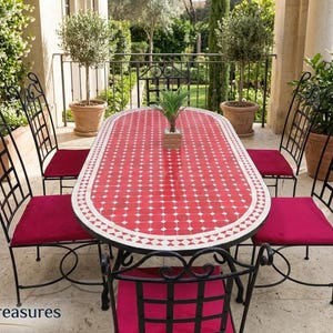 Puede incluir: Un juego de comedor al aire libre con una mesa de mosaico roja, borde blanco y sillas de hierro forjado negro con cojines rojos. La mesa ovalada está rodeada de seis sillas. La escena está ambientada en un patio.
