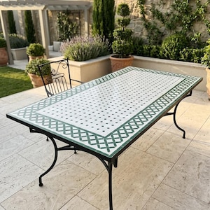 May include: A rectangular outdoor table featuring a white and green mosaic tile top with a geometric pattern and a black metal frame with curved legs. The table is accompanied by a matching black metal chair with a decorative backrest.