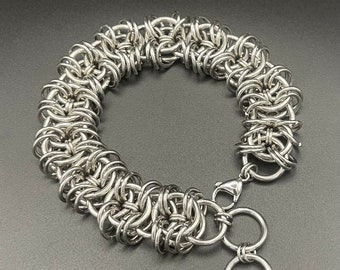 May include: A silver chainmail bracelet with a clasp closure. The bracelet is made of many small, interconnected metal rings.