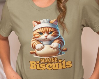 May include: A green t-shirt with a cartoon cat wearing a chef's hat and rolling out dough. The text on the shirt says "Making Biscuits" with a heart on either side of the word "Making".