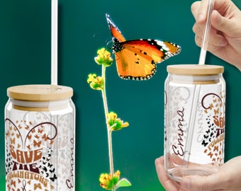 May include: Two clear glass tumblers with bamboo lids and straws. Both tumblers have a design of butterflies and the text "Save the Pollinators". One tumbler has the name "Emma" written on it.