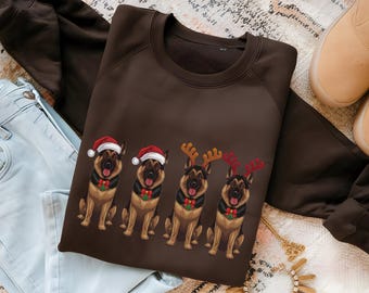 May include: A brown sweatshirt featuring a graphic of four German Shepherds. The dogs are wearing Santa hats and reindeer antlers, with festive collars. The sweatshirt is folded on a patterned rug, with jeans and boots visible.