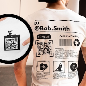May include: White t-shirt with a black and white design on the back. The design includes a QR code, the text "DJ @Bob.Smith", "SCAN ME", and a list of "INGREDIENTS" for a DJ, including creativity, rhythm, music knowledge, energy, technical skills, crowd awareness, adaptability, attention to detail, confidence, timing, mixing skills, and passion for music.